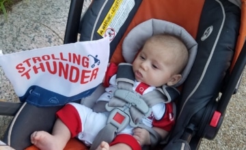 An infant in a stroller with a Strolling Thunder flag