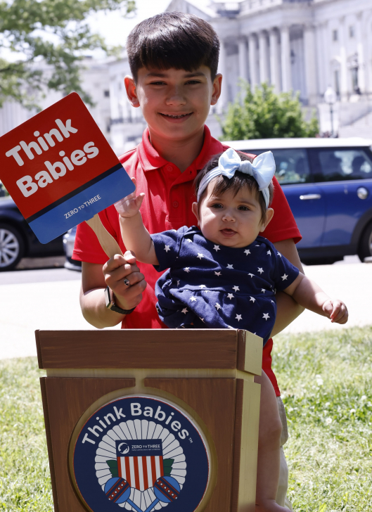 A young child holding an infant in front of the Capitol building in Washington, D.C.