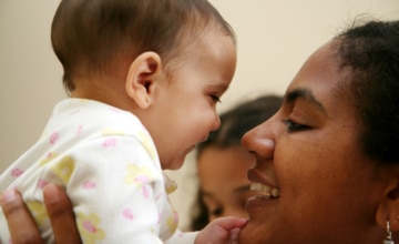 A mother holding up her infant to her face and smiling